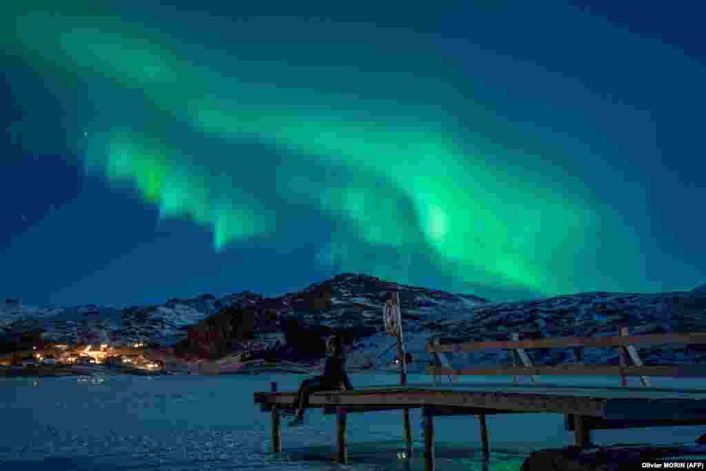 A woman sits on a pier watching the Northern Lights (aurora borealis) on the Lofoten Islands in northern Norway. (AFP/Olivier Morin)