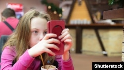  Маленькая девочка сидит в ресторане на зимних каникулах, пользуется мобильным телефоном, развлекается.