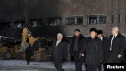 Нұрсұлтан Назарбаев (сол жақтан үшінші) өртеніп кеткен ғимараттың қасында жүр. Жаңаөзен. 22 желтоқсан, 2011 жыл. 