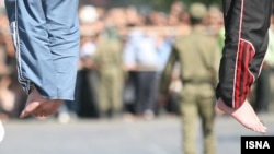 Iran -- Feet of two executed men, at the background a policeman, undated