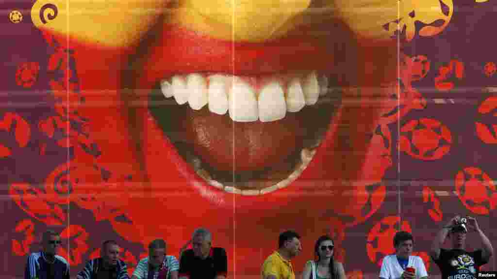 Soccer fans wait in front of a billboard depicting a face painted in the Spanish national colors before the start of the final.