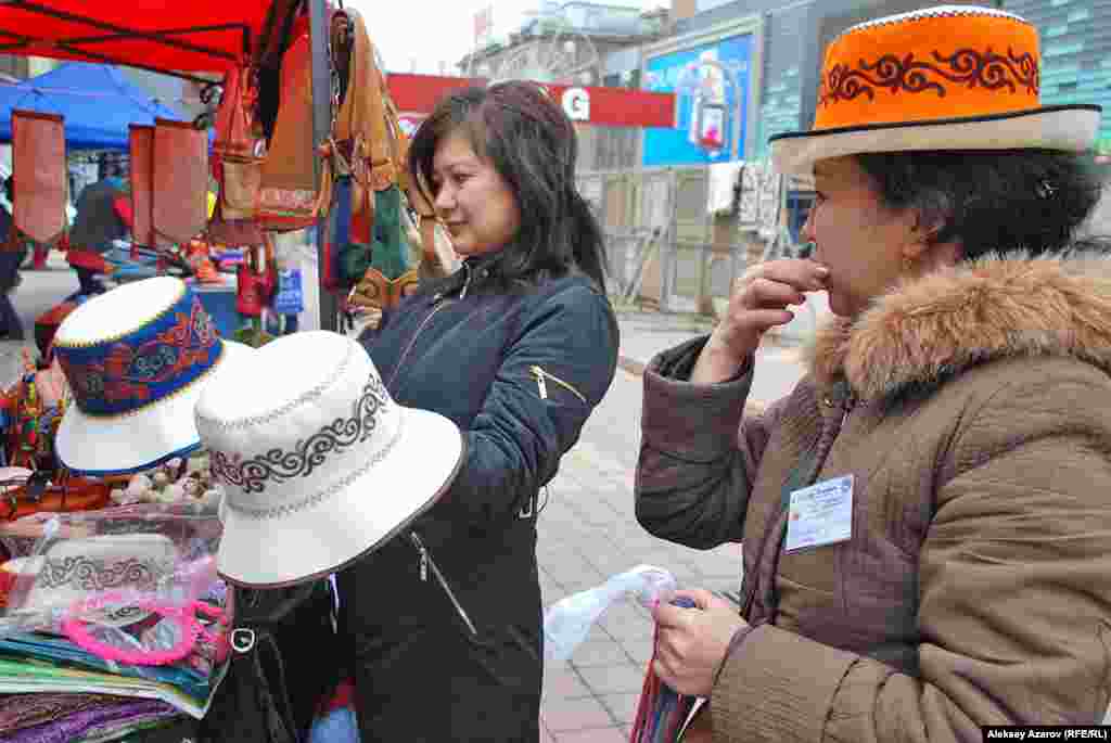 Посетительница фестиваля никак не может определиться с выбором шляпы кыргызской ремесленницы. И даже спросила совета у фотографировавшего репортера Азаттыка.