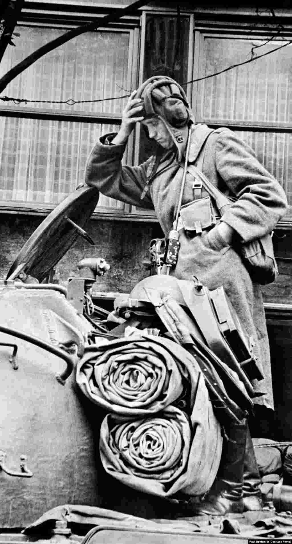 A weary occupying soldier leans on the lid of his tank. 