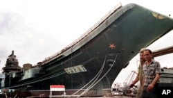 Workers walk in front of the aircraft carrier "Varyag" at a dockyard in Mykolayiv in May 1997, before its transfer to Chinese hands.