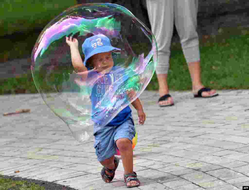 A boy plays with a soap bubble in one of Kyiv&#39;s parks on a hot day in the Ukrainian capital. (AFP/Sergei Supinsky)