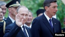 On a trip to Slovenia, Russian President Vladimir Putin (left) waves as he attends the centenary commemoration of a Russian chapel with Slovenian President Borut Pahor (right) on July 30,