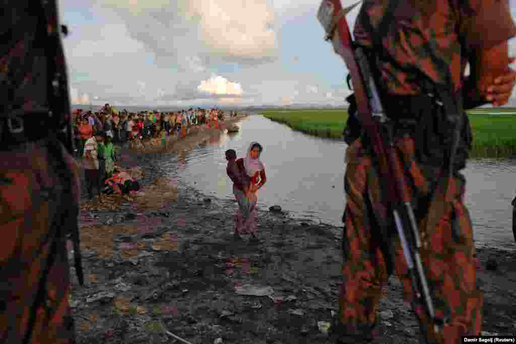 Bangladeshi border guards watch as Rohingya refugees, who fled from Burma, make their way through a rice field after crossing the border at Palang Khali. (Reuters/Damir Sagolj)