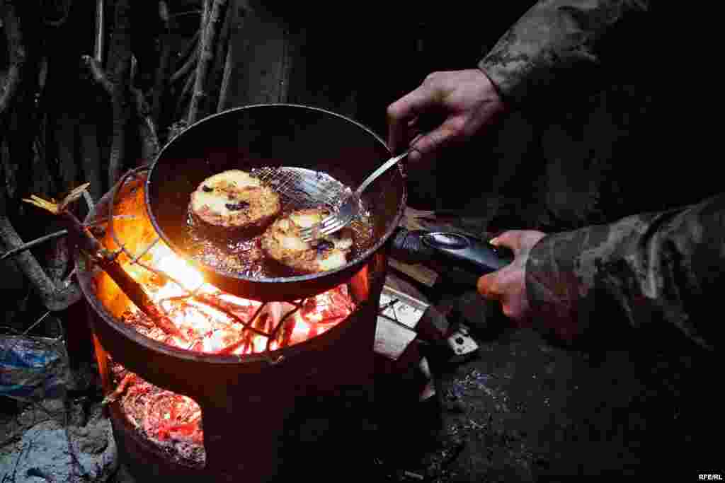 A soldier has made himself buns soaked in egg yolk for lunch. The buns are are heated over a wood-burning stove after being soaked.