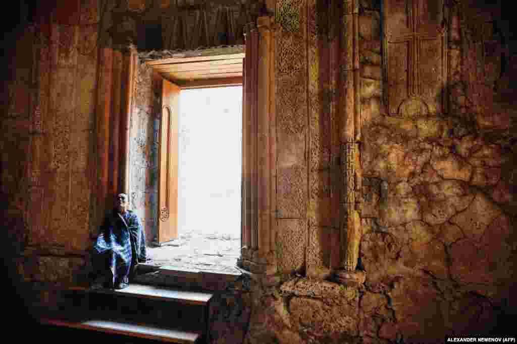 A woman sits at an entrance to the monastery.