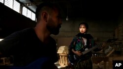 In this July 26, 2018 photo, Afghan musicians Hakim Ebrahimi, left, and Soraya Hosseini, members of the Arikayn rock band, play music at a furniture workshop on the outskirts of Tehran, Iran. Like others in Iran's vibrant arts scene, Afghan musicians must