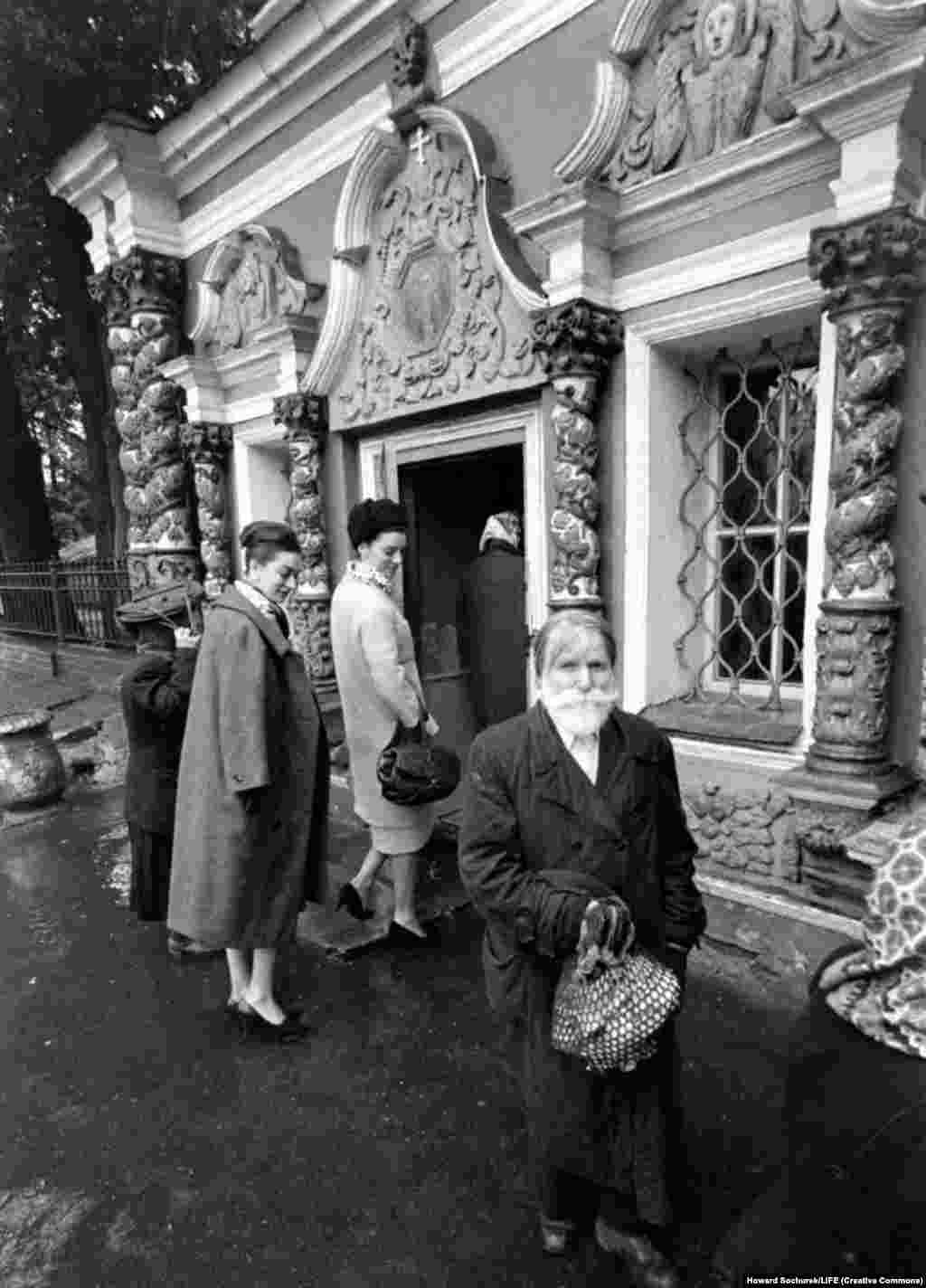 The foreign visitors check out a dapper Soviet gentleman as they head into a church on a rainy day.