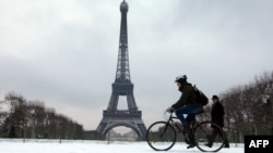 France -- A man rides a bicycle past the Eiffel Tower in Paris, 13Jan2010