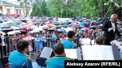 Военный оркестр играет на праздновании Дня Победы в Алматы. Перед сценой – сотни людей под зонтами, в этот момент уже лил дождь. 9 мая 2015 года.