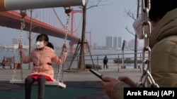 A girl wears a face mask as she plays on a swing in Wuhan, China, where the virus was first identified.