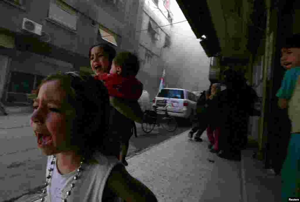 Four-year-old Ghazal (L) runs away with seven-year-old Judy, who is carrying 8-month-old Suhair, after the shelling of a Red Crescent convoy in Damascus, Syria, on May 6, 2015. (Reuters//Bassam Khabieh)