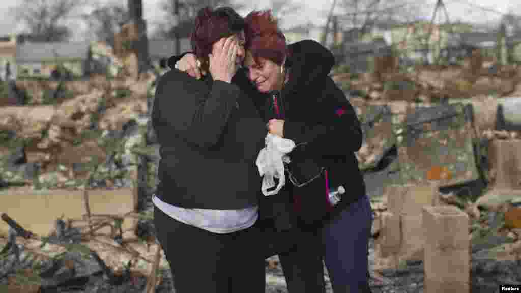 Două vecine, Lucille Dwyer și Linda Strong, &icirc;mbrățiș&icirc;ndu-se printre casele dăr&icirc;mate de uraganul Sandy &icirc;n suburbia Queens a New York-ului. (Reuters/Shannon Stapleton)