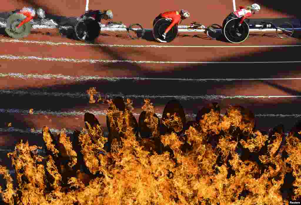 Competitors are seen through the Paralympic flame as they race in the women&#39;s 5000-meter heats at the Olympic Stadium on August 31 during the 2012 Paralympic Games. (Reuters/Toby Melville)