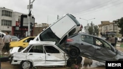 People stand near a pile of damaged cars after a flood hit the city of Shiraz on March 25.