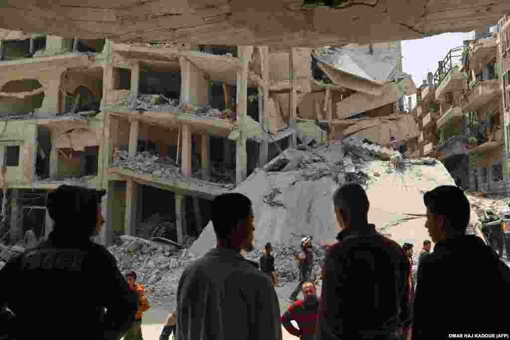 People watch as members of the Syrian Civil Defense, also known as the White Helmets, search the rubble of a collapsed building following an explosion in the town of Jisr al-Shughur, in the west of the mostly rebel-held Syrian province of Idlib, on April 24. Over a dozen people, all but two civilians, were killed. The cause of the blast was not immediately clear. (AFP/Omar Haj Kadour)​