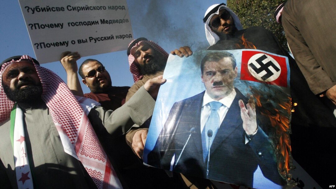 Newly elected Kuwaiti deputy Walid Tabtabai (left) holds a burning portrait of Russian President Dmitry Medvedev during a protest in front of the Russian Embassy in Kuwait City on February 6.