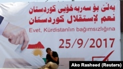 A man talks on the phone infront of a banner urging people to vote for the 25th independence referendum in Kirkuk, September 10, 2017