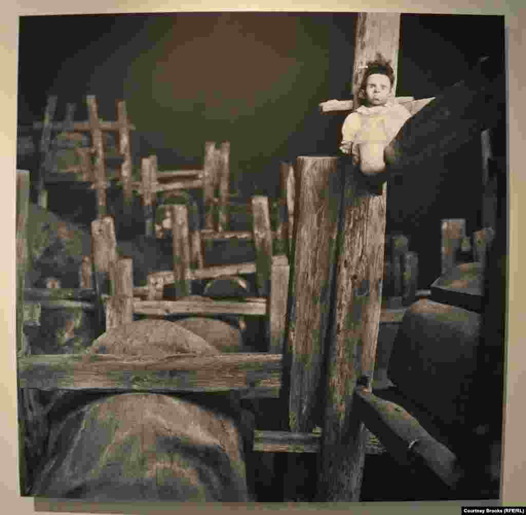 A doll perched atop a pile of wood frowns.