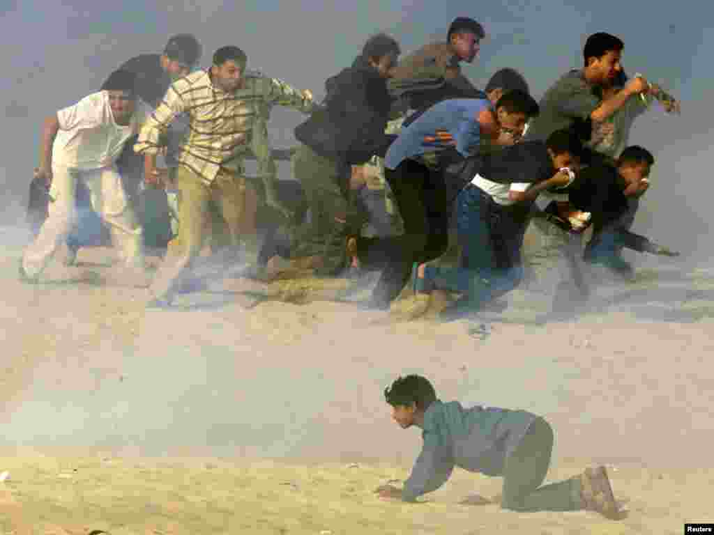 Palestinians run to escape, while one crawls, as Israeli soldiers fire teargas during Palestinian-Israeli clashes in the south Gaza Strip town of Khan Yones October 20, 2000. The ongoing conflict in Isreal has so far this year seen 281 Palestinians killed. REUTERS