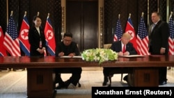Лідер КНДР Кім Чен Ин (за столом ліворуч) та президент США Дональд Трамп підписують угоду за результатами саміту в Сингапурі, 12 червня 2018 року.