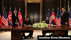 Cингапурдун Сентоса аралында АКШнын президенти Дональд Трамп жана Түндүк Кореянын лидери Ким Чен Ын документке кол коюп жатышат. 12-июнь, 2018-жыл.
