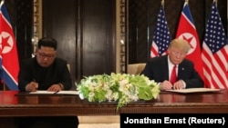 АҚШ президенті Дональд Трамп (оң жақта) пен Солтүстік Корея лидері саммит қортындысы бойынша құжатқа қол қойып отыр. Сингапур, 12 маусым 2018 жыл.