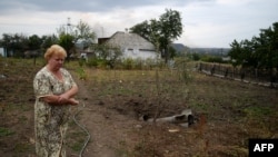 Ukraine -- A villager walks by a unexploded rocket that landed on her backyard in Troitsko-Khartsyzk, 30 Km east of Donetsk, August 28, 2014