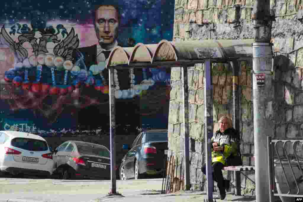 A woman waits at a bus stop in front of a graffito depicting Russian President Vladimir Putin on a building in Sevastopol on the Russian-occupied Ukrainian peninsula of Crimea. (AFP)