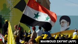 Lebanese Hezbollah supporters wave a Syrian flag under a huge portrait of Iran's supreme leader, Ayatollah Ali Khamenei, during a rally in the southern town of Bint Jbeil on May 25, 2012