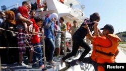 Сотрудник пограничной службы Турции помогает беженцам из Сирии сойти с корабля в порту города Кесме. 11 августа 2015 года.