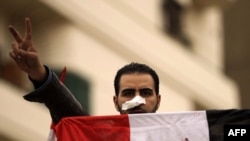 An antigovernment protester flashes the victory sign while holding the national flag in Tahrir Square in Cairo.