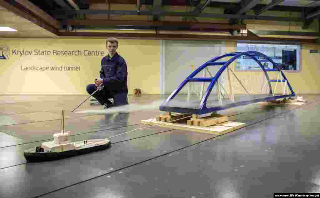 An engineer watches a scale model of the bridge being towed through a wind tunnel.