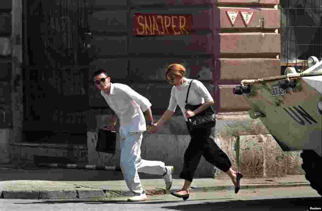 A young couple runs across the infamous Sniper Alley in Sarajevo in 1995. Snipers in the surrounding hills, combined with the relentless mortar rounds bursting on the streets, made even a trip to collect water a perilous task during the 44 months of the siege.