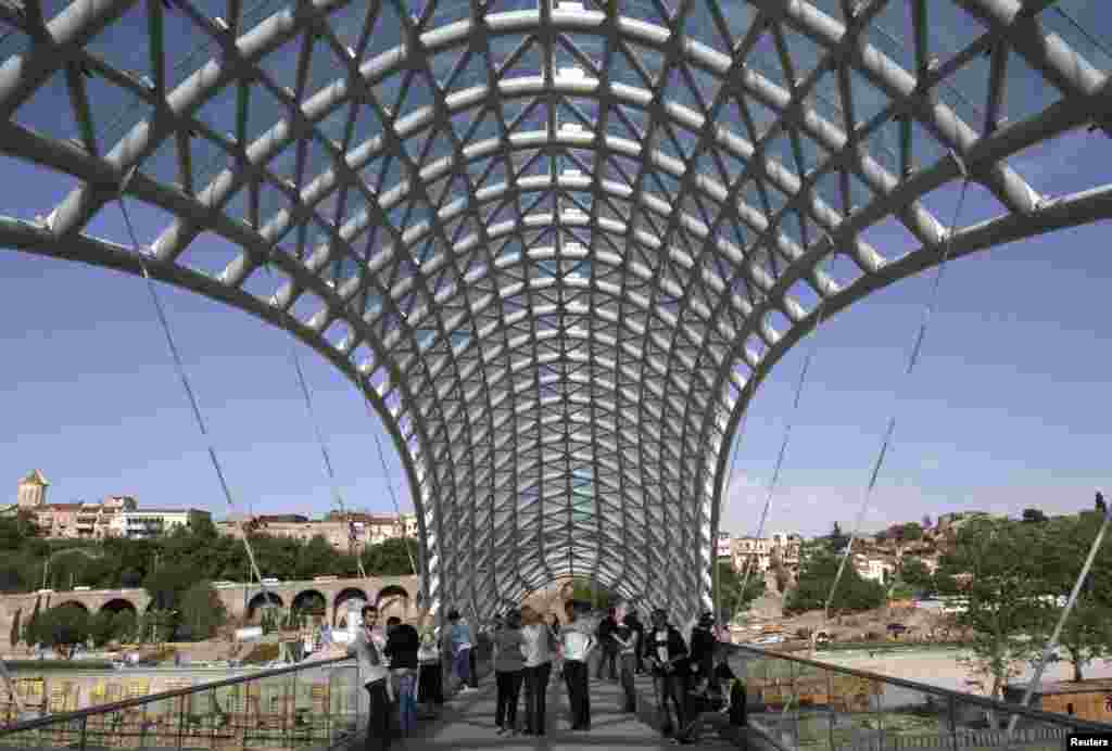 Pedestrians walk across the recently built Bridge of Peace, which traverses the Kura River in Tbilisi&#39;s old town.