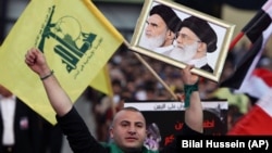 یک هوادار گروه حزب‌الله لبنان در حالی که عکس آیت‌الله خمینی و خامنه‌ای را در دست دارد، به نفع این گروه شعار می‌دهد.