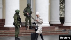 Женщина проходит мимо вооруженных людей в военной форме без опознавательных знаков, блокировавших аэропорт Симферополя. 28 февраля 2014 года.
