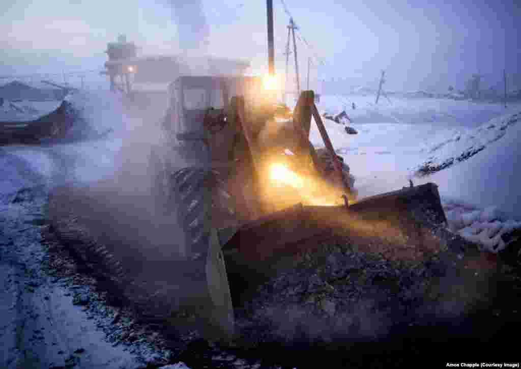 A bulldozer dumps coal ash burned by the village&#39;s heating plant. The plant works through the day and night to pump hot water through the pipes of the village.