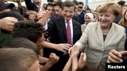 Turkish Prime Minister Ahmet Davutoglu (center) and German Chancellor Angela Merkel are greeted by refugees in Nizip refugee camp on April 23.