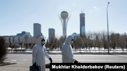Сотрудники в защитной одежде на санобработке улицы в центре казахстанской столицы. Нур-Султан, 24 марта 2020 года.