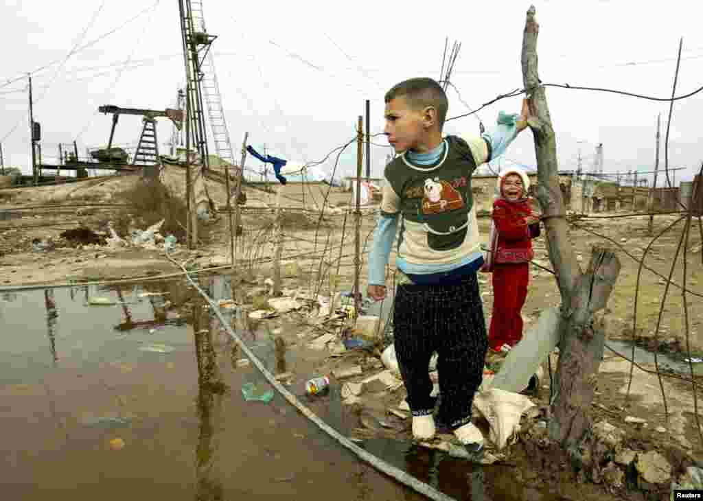 A boy and a girl stand near nodding donkeys in a refugee camp outside Baku.&nbsp;