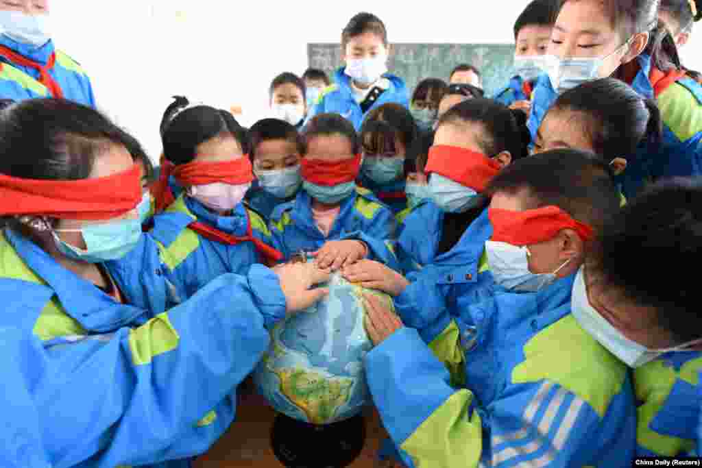 Учні початкових класів у масках торкаються глобусу із заплющеними очима під час заняття до прийдешнього Дня Землі. Китай, 21 квітня 2020 року