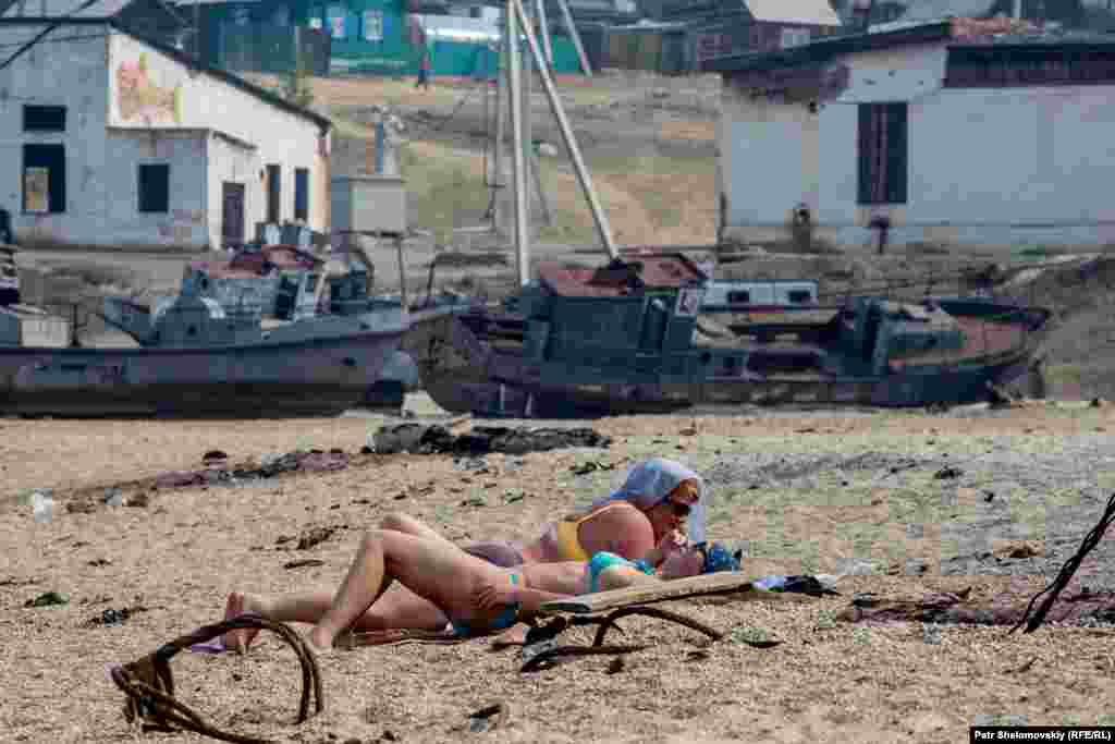 Tourists sunbathing in front of abandoned fishing vessels. The island was once home to a fish processing plant, with labor provided by prisoners of the gulag system. Now former fishing vessels are mainly used to transport summer visitors.