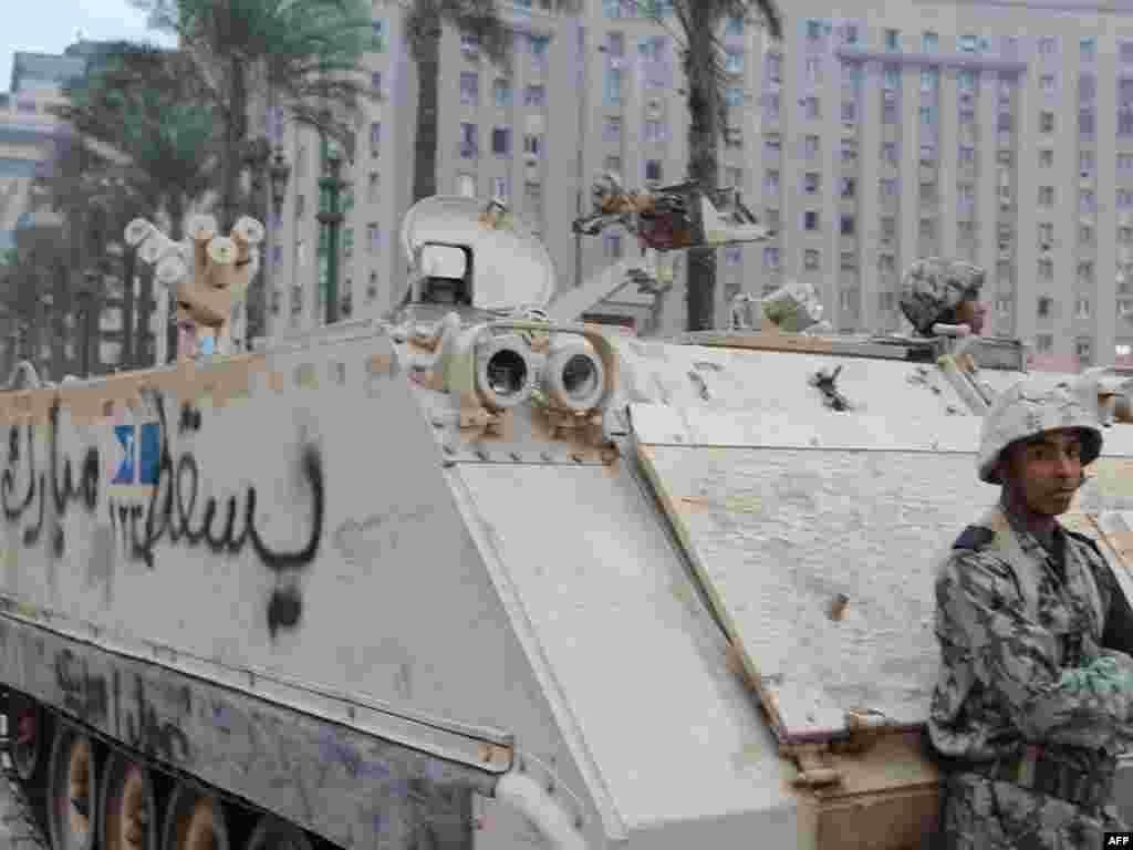 A soldier stands guard beside an armored vehicle with the slogan "Down Mubarak" painted on it.