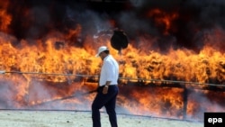 Iran -- An Iranian policeman walks past a cloud of smoke rising from a pile of drugs set on fire during an incineration ceremony of some 50 tons of illicit drugs in an annual ritual in Tehran, June 26, 2014