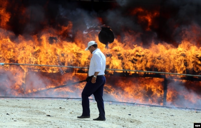 An Iranian policeman walks past a cloud of smoke rising from a pile of drugs that was set on fire during an incineration ceremony for some 50 tons of illicit narcotics seized by the authorities. (file photo)