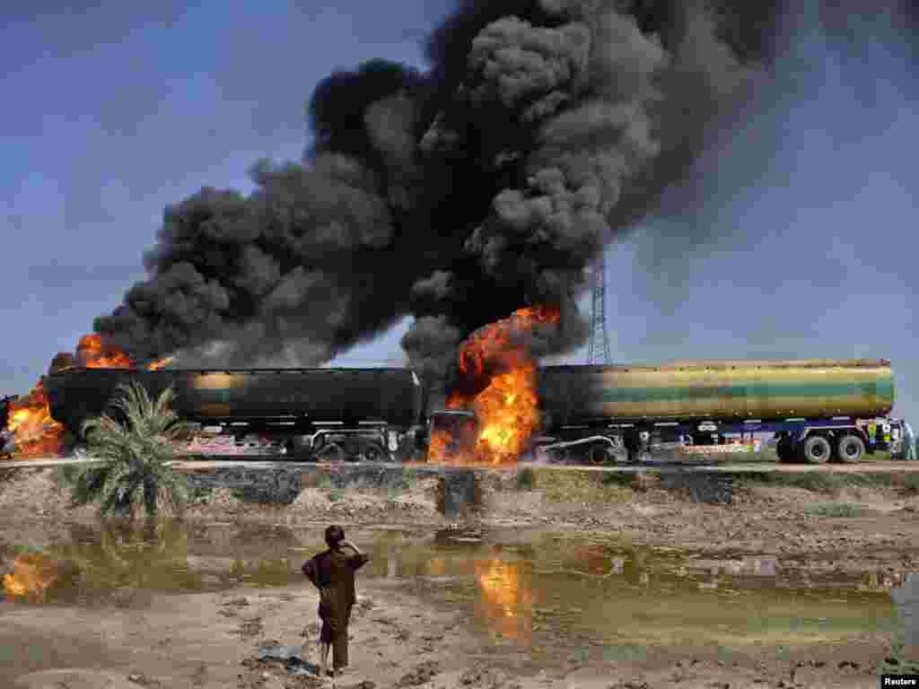 A boy looks at a plume of smoke rising from fuel trucks after they were attacked by unidentified gunmen on a highway near Shikarpur, Pakistan. (Photo by Nadeem Soomro for Reuters)